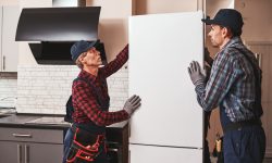 Moving again. Young men mechanics moving refrigerator